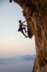 Poster Young woman climbing challenging route at sunset © Andrey Bandurenko