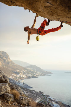 Young man climbing challenging route in cave against beautiful view of coast