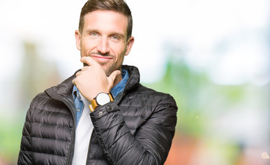 Handsome man wearing winter coat looking confident at the camera with smile with crossed arms and hand raised on chin. Thinking positive.