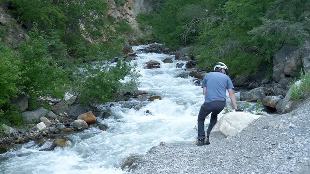 Cyclist stops along a mountain trail to take pictures of a rushing river