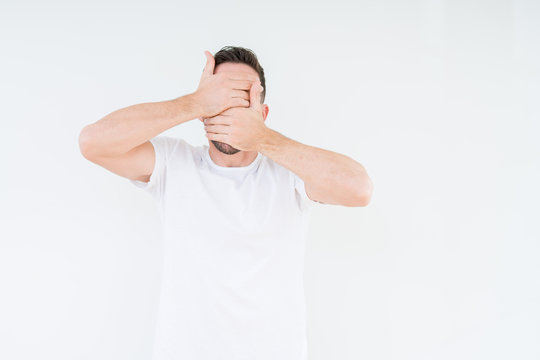 Young handsome man wearing casual white t-shirt over isolated background Covering eyes and mouth with hands, surprised and shocked. Hiding emotion