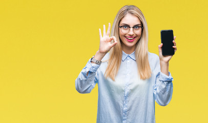 Young beautiful blonde business woman showing screen of smartphone over isolated background doing ok sign with fingers, excellent symbol