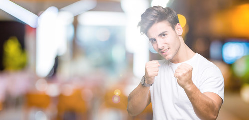 Young handsome man wearing white t-shirt over isolated background Ready to fight with fist defense gesture, angry and upset face, afraid of problem