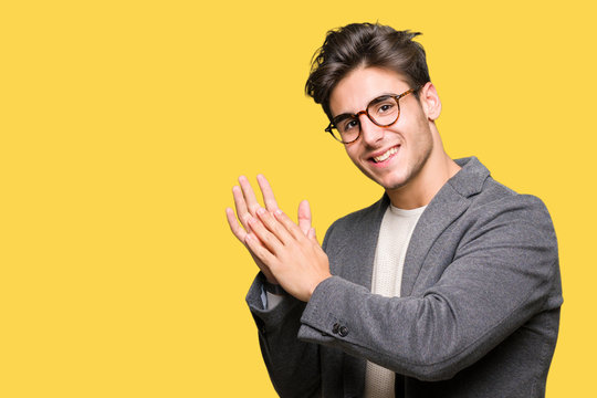 Young business man wearing glasses over isolated background Clapping and applauding happy and joyful, smiling proud hands together