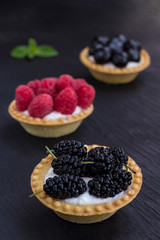 Basket-shaped cookies with raspberry, blueberry and blackberry berries. Black background.