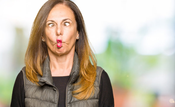 Beautiful middle age woman wearing winter vest making fish face with lips, crazy and comical gesture. Funny expression.
