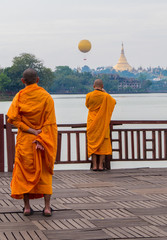 Buddhist monks looking at the Shwedagon Pagoda and the Mingalarbar Hot Air Balloon from the Kandawgyi Lake. In Yangon, Myanmar