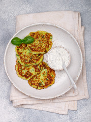 Fritters of zucchini with fresh parsley and Basil. Delicatessen vegetable pancakes with sauce from sour cream and dill. Selective focus
