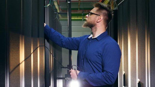 Man plugs a wire to a server computer. IT support concept.