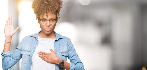 Beautiful young african american woman wearing glasses over isolated background Swearing with hand...
