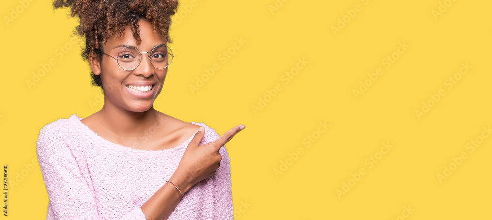 Wall mural Beautiful young african american woman wearing glasses over isolated background cheerful with a smile of face pointing with hand and finger up to the side with happy and natural expression on face