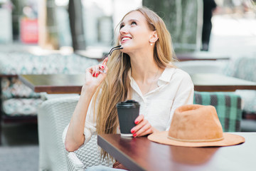 Cheerful smiling blond woman sits in a street cafe and drinks coffee