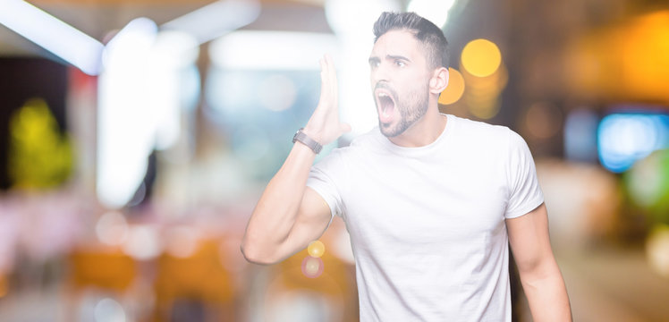 Young man wearing casual white t-shirt over isolated background shouting and screaming loud to side with hand on mouth. Communication concept.