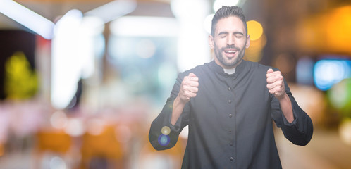 Young Christian priest over isolated background excited for success with arms raised celebrating...