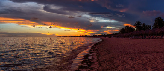 Fototapeta na wymiar Beautiful Panoramic view of a sandy beach, Playa Ancon, on the Caribbean Sea in Triniday, Cuba, during a dramatic cloudy sunset.
