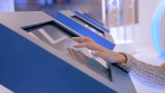 Education and technology concept - woman using interactive touchscreen display of electronic kiosk at modern museum or exhibition