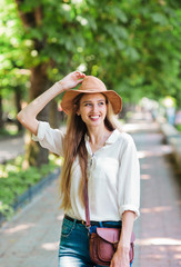 Cheerful blond woman tourist in casual style clothes and felt hat walking through the summer city. Emotional fashion portrait