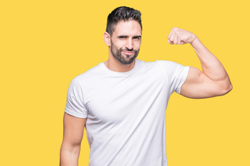 Handsome man wearing white t-shirt over yellow isolated background Strong person showing arm...