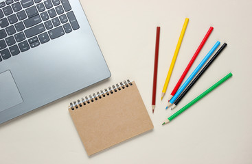 Back to school minimalistic concept. Laptop, color pencils, notebook on a beige background. Top view