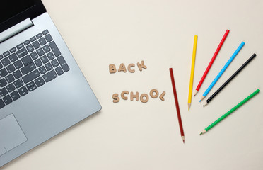 Back to school minimalistic concept. Laptop, color pencils on a beige background. Slogan back school.Top view
