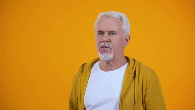 Gray-haired pensioner showing face-palm gesture against orange background, fail