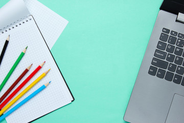 Back to school minimalistic concept. Laptop, color pencils, notebook on blue background.