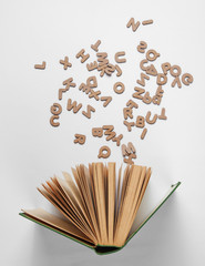 Open old book with scattered letters on white background. Top view, minimalism