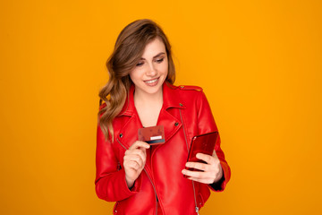 Naklejka premium Pretty girl in red clothes holding phone and credit card isolated over the bright yellow background