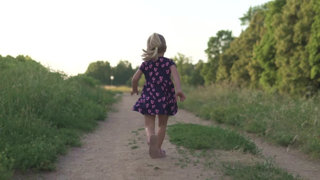 Beautiful little girl running across the field at sunset. Back view. Baby smiles and laughs. Danger, the child runs off to the road with cars