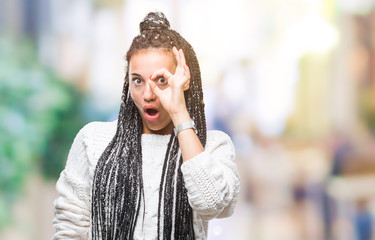 Young braided hair african american girl wearing sweater over isolated background doing ok gesture shocked with surprised face, eye looking through fingers. Unbelieving expression.