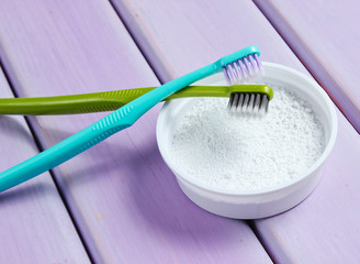 Two toothbrushes, tooth powder on purple wooden background. Minimalism oral hygiene concept. Top...