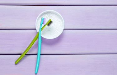 Two toothbrushes, tooth powder on purple wooden background. Minimalism oral hygiene concept. Top view