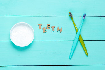 Two toothbrushes, tooth powder on blue wooden background with word teeth. Minimalism oral hygiene...