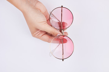 female hand holding pink round sunglasses with light background