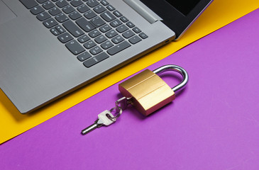 Computer protection concept, internet security. Laptop and lock on purple yellow paper background