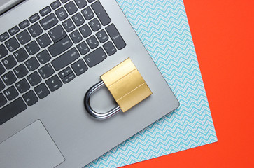 Computer protection concept, internet security. Laptop and lock on orange blue paper background
