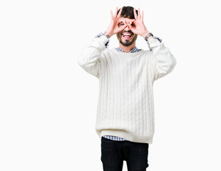 Fototapeta premium Young handsome man wearing winter sweater over isolated background doing ok gesture like binoculars sticking tongue out, eyes looking through fingers. Crazy expression.