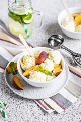  Homemade peach ice cream with mint and fresh peach slices in a plate on a gray background