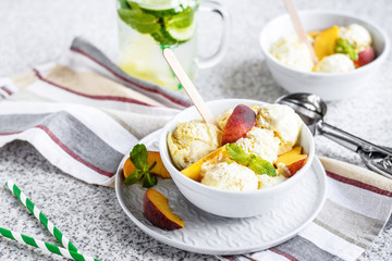  Homemade peach ice cream with mint and fresh peach slices in a plate on a gray background