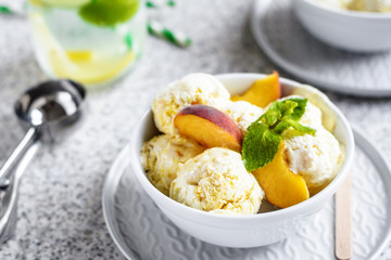  Homemade peach ice cream with mint and fresh peach slices in a plate on a gray background