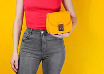 Slim woman holding a yellow leather bag on yellow background. Crop photo, studio shot