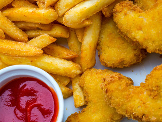Fresh french fries and chicken nuggets served with tomato sauce on white plate
