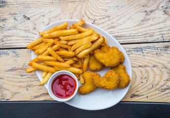 Fried crispy chicken nuggets and french fries with ketchup on white wooden board