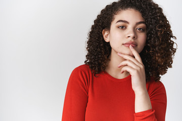 Fototapeta na wymiar Close-up thoughtful hispanic young stylish pondering girl dark curly-haired touch lip thinking curiously look camera gazing interest amusing exhibition, standing white background daydreaming