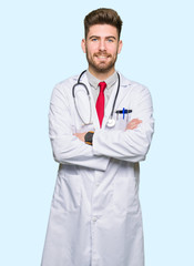 Young handsome doctor man wearing medical coat happy face smiling with crossed arms looking at the camera. Positive person.