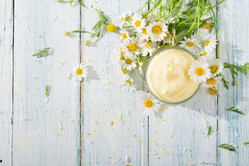 chamomile flowers and baby cream on white wooden table, directly above