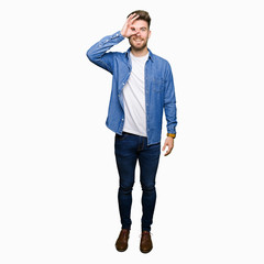 Fototapeta premium Young handsome blond man wearing casual denim jacket doing ok gesture with hand smiling, eye looking through fingers with happy face.