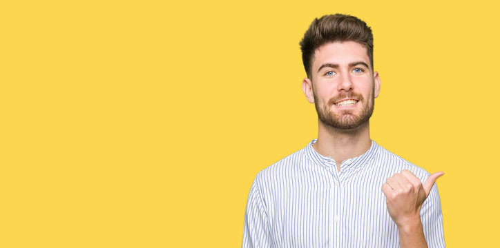 Young handsome man smiling with happy face looking and pointing to the side with thumb up.