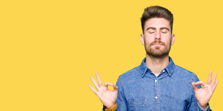 Young handsome blond man wearing casual denim shirt relax and smiling with eyes closed doing meditation gesture with fingers. Yoga concept.
