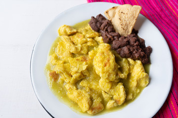 Mexican scrambled eggs in green sauce also called "al abañil" with beans on white background